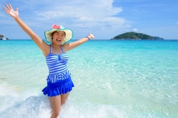 Beautiful woman in a swimwear striped blue hat standing with arms outstretched to life carefree at sea and sky in summer on the beach of Miang Island, Mu Ko Similan National Park, Phang Nga, Thailand