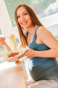 Photo of pregnant woman eating huge portion of pasta with tomato sauce