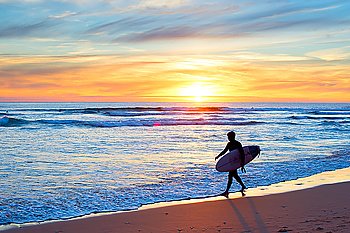 Surfer with surfboard on the ocean beach at sunset.