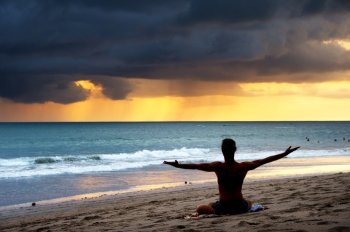 Silhouette of a man doing yoga exercise on the beach. Bali island, Indonesia