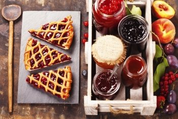 Fruit and berry jam and pieces of fruit tart on a rustic background