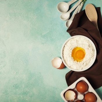 Baking background with flour, eggs and kitchen tools on blue rustic table. Top view. Flat lay style.