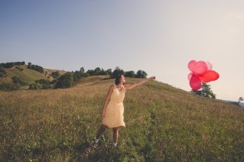 Adult beautiful girl playing with red balloons on the field