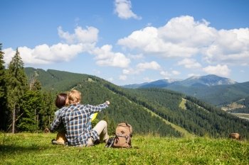 Travelling couple sitting on the alpine meadow and looking at the map