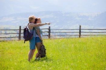 Couple hikers walking at the summer meadow and looking around countryside view