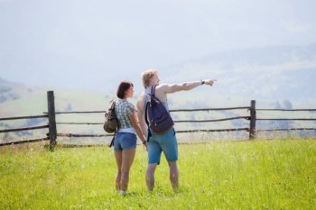 Couple hikers walking at the summer meadow and looking around countryside view