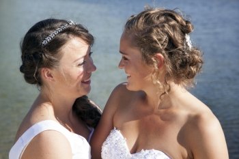 just married happy lesbian couple in white dress look each other happily in the eyes at waterfront on sunny day