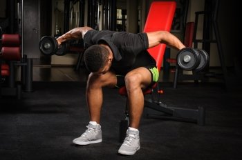 handsome young african descent mixed race man doing Seated Bent Over Dumbbell Reverse Fly workout in gym. Young man doing Seated Bent Over Dumbbell Reverse Fly workout in gym
