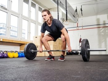 Photo of a handsome young man lifting a heavy barbell for a clean and jerk movement at the gym.
