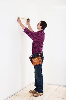 Young worker handyman with measuring tape near the wall in room
