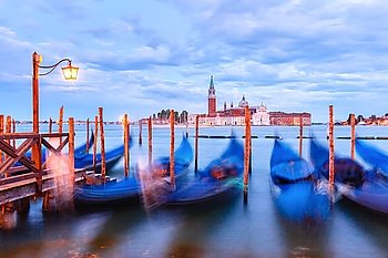 Gondolas moored by Saint Mark square with San Giorgio di Maggiore church in the background  during twilight blue hour, Venice, Italia