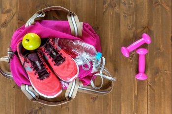 Women's sports bag with objects and clothes for a workout on a dark floor view from above