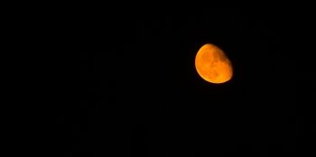 The moon takes on an orange hue in a dark night