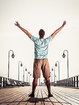 Man on pier with raised hands arms. Freedom.. Man tourist on pier with raised hands arms. Guy enjoying summer travel vacation by sea. Fashion. Happiness and freedom concept.