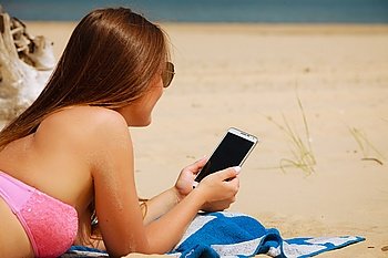 Woman on beach texting on smartphone.. Communication concept. Young woman spending time on summer beach texting messages on smartphone. Girl using mobile phone.
