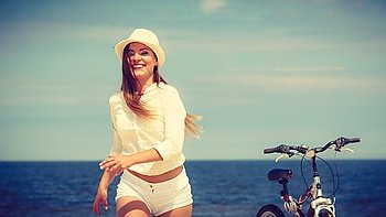 Girl with bike on beach.. Sport and recreation. Young girl in straw hat resting after cycling on beach. Smiling tourist spending time on seaside. Leisure in summer.