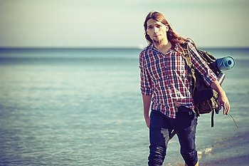 Man hiker backpacker walking with backpack on sea shore at sunny day. Adventure, summer, tourism active lifestyle. Young long haired guy tramping