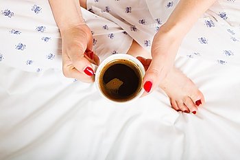Woman relaxing at cozy home atmosphere on the bed. Female with red nails manicure holds cup of coffee in hands enjoying comfort, top view