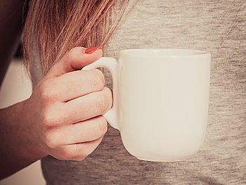 woman on bed with cup of coffee. Woman relaxing at cozy home atmosphere on the bed. Female with red nails manicure holds cup of coffee in hands enjoying comfort