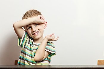 Free time, fun and expression. Little boy play indoors make silly gestures emotions hand in air. Blonde child in striped shirt sit white wall.