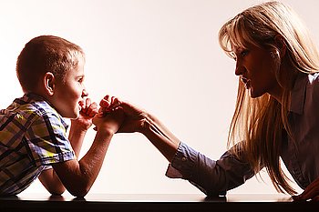 Mother and son arm wrestle sit at table.. Spending time with family fun and family bonds. Mother and son arm wrestle and have fun indoors.