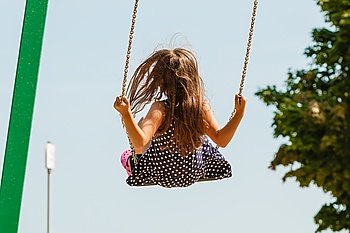Girl swinging on swing-set.. Have fun and leisure concept. Long haired enjoyable girl swinging outdoor in garden playground. Lovely child playing on swing-set.