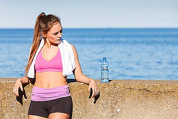 Woman in sportswear takes a break to rehydrate drinking water from plastic bottle, resting after sport workout outdoor by seaside