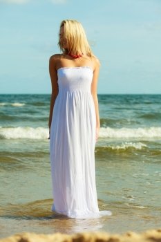 Attractive blonde woman on the beach.. Holidays beach summer and blonde lady. Attractive woman spending free time on the beach. Female wearing white dress and red necklace. 