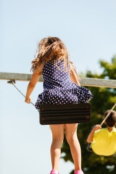 Girl swinging on swing-set.. Have fun and leisure concept. Long haired enjoyable girl swinging outdoor in garden playground. Lovely child playing on swing-set.