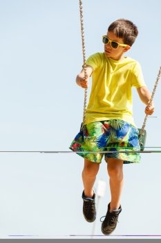 Boy playing swinging by swing-set.. Rest and relax for children. Little boy in sunglasses resting swinging outdoor. Adorable child having fun playing in playground.