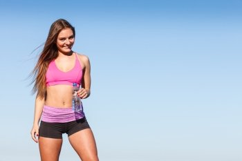 Woman in sportswear takes a break to rehydrate drinking water from plastic bottle, resting after sport workout outdoor