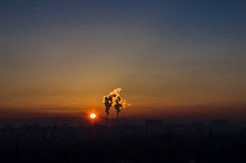 Chimneys and dark smoke over  factory at sunset