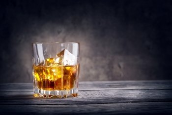 Faceted glass of whiskey with ice on dark background. Faceted glass of whiskey with ice