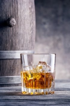 Round glass of whiskey with ice cubes against the background of wooden barrels