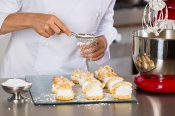 Pastry chef decorating with icing sugar some profiteroles