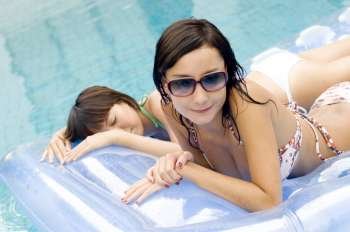High angle view of two young women lying on a pool raft in a swimming pool
