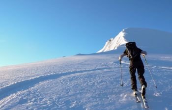 backcountry skier hiking towards a high alpine peak in Switzerland on a beautiful winter day