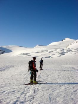 two male backcountry ski mountaineers head towards a high alpine peak over a long glacier between Saas Fee and Zermatt