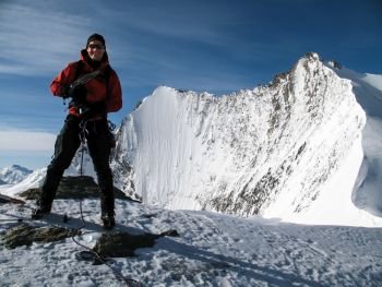 male mountain climber smiling and laughing on the summit of a high alpine peak with a great backdrop of fantastic mountains