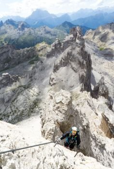 young handsome male climber on a steep and exposed rock face climbs a Via Ferrata in Alta Badia in the South Tyrol