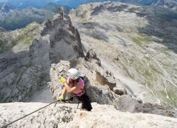 Horizontal view of attractive brunette female climber on a steep and exposed Via Ferrata in the Dolomites pointing to the distance