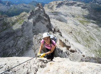 Horizontal view of attractive brunette female climber on a steep and exposed Via Ferrata in the Dolomites