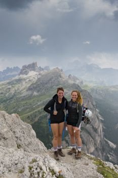 two attractive young female mountain climbers standing on a mountain peak and smiling