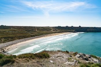 A view of the Plage de Pen Hat beach and bay with many surfers surfing on  a beautiful summer day on the coast of Brittany
