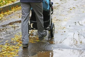 Walking father with child in the fresh air. A man carries a baby carriage on an asphalt road, through puddles.