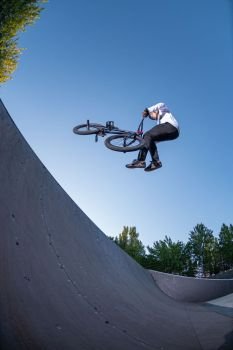 Bmx stunt performed at the top of a quarter pipe ramp on a skatepark.