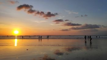 Silhouettes of people enjoying dramatic sunset at Kuta beach in Bali, Indonesia