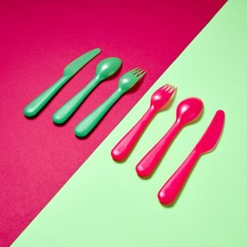 Diagonal pattern of plastic multicolored tableware on a duotone background with copy space.. Kids plastic colorful cutlery on a duotone background.