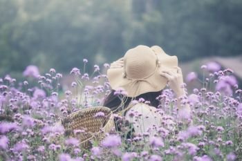 Woman wearing sun hat and bamboo basket visiting Verbena flower field. Image with film camera filter.