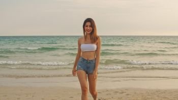 Asian woman walking on sand beach. Young happy female in bikini relax and fun walking near tropical sea when sunset while holiday, vacation, summer trip concept.